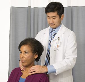 Médico palpando el cuello de una mujer para examinar la glándula tiroidea.